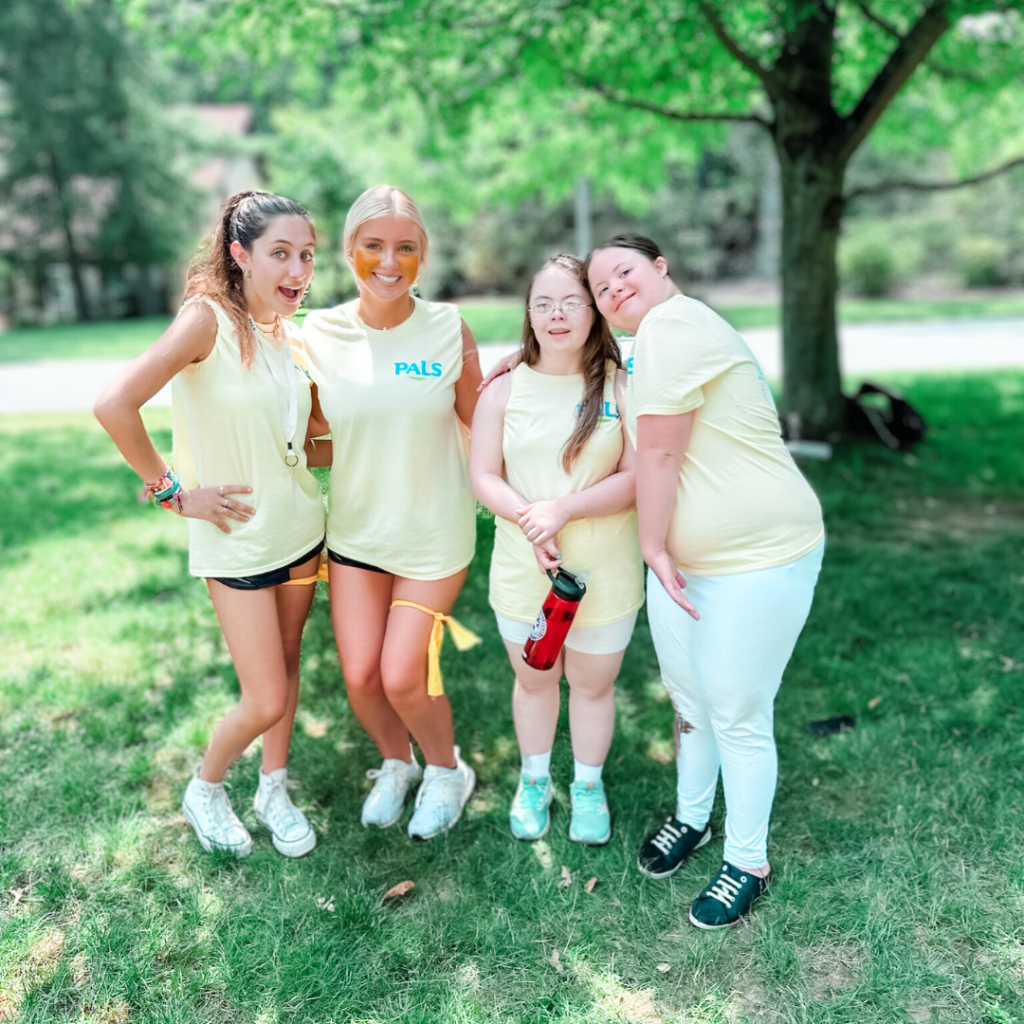 photo of Penny standing with 3 friends outside at Camp PALS. They are all wearing yellow t-shirts with the PALS logo