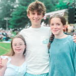 photo of Penny, William, and Marilee standing outside smiling at the camera with a seated crowd blurred in the background