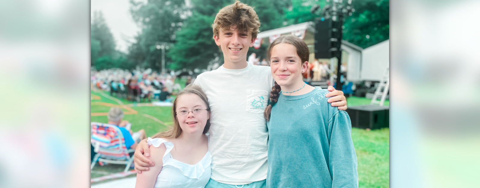 photo of Penny, William, and Marilee standing outside smiling at the camera with a seated crowd blurred in the background