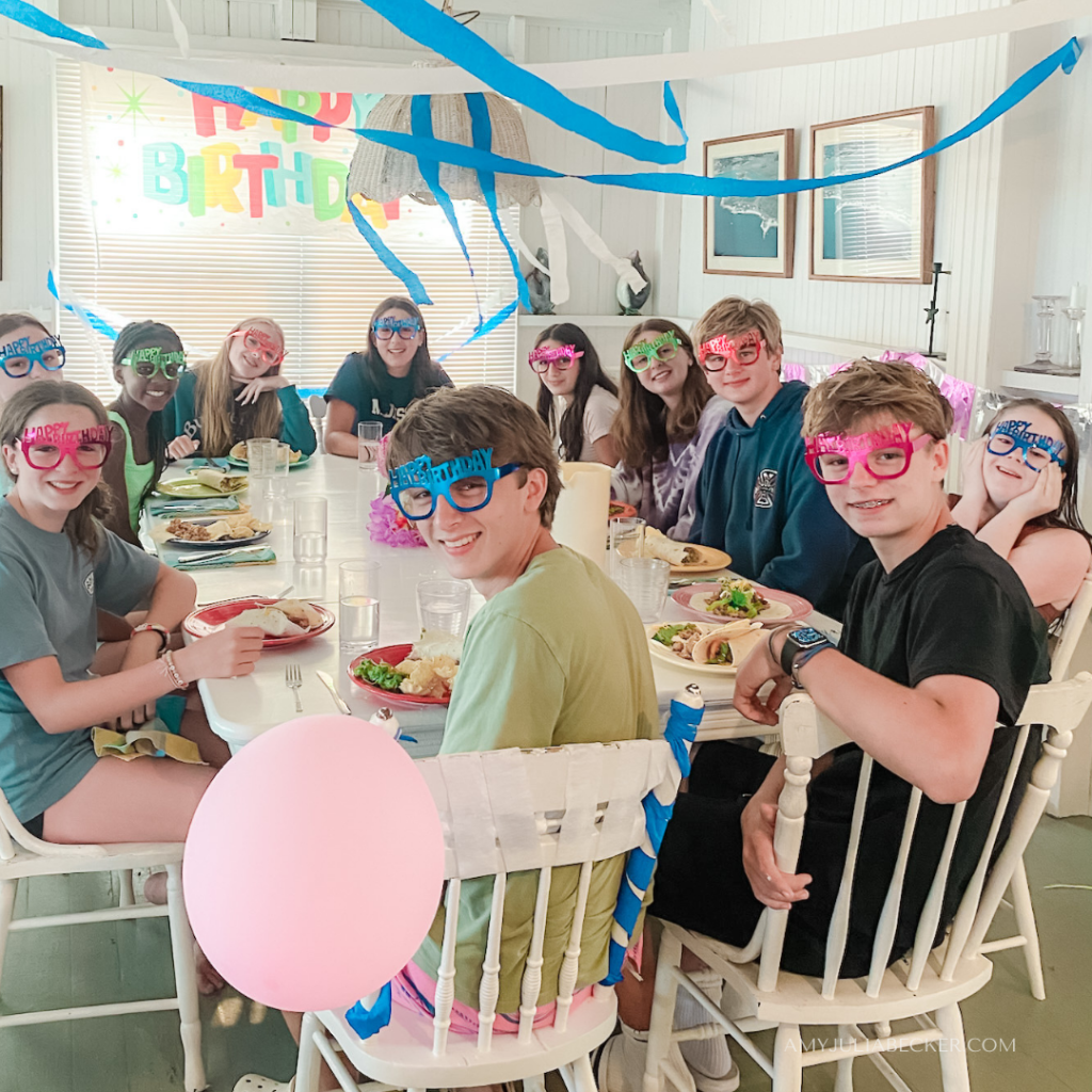 photo of William with family and friends sitting at a large white table for a birthday party
