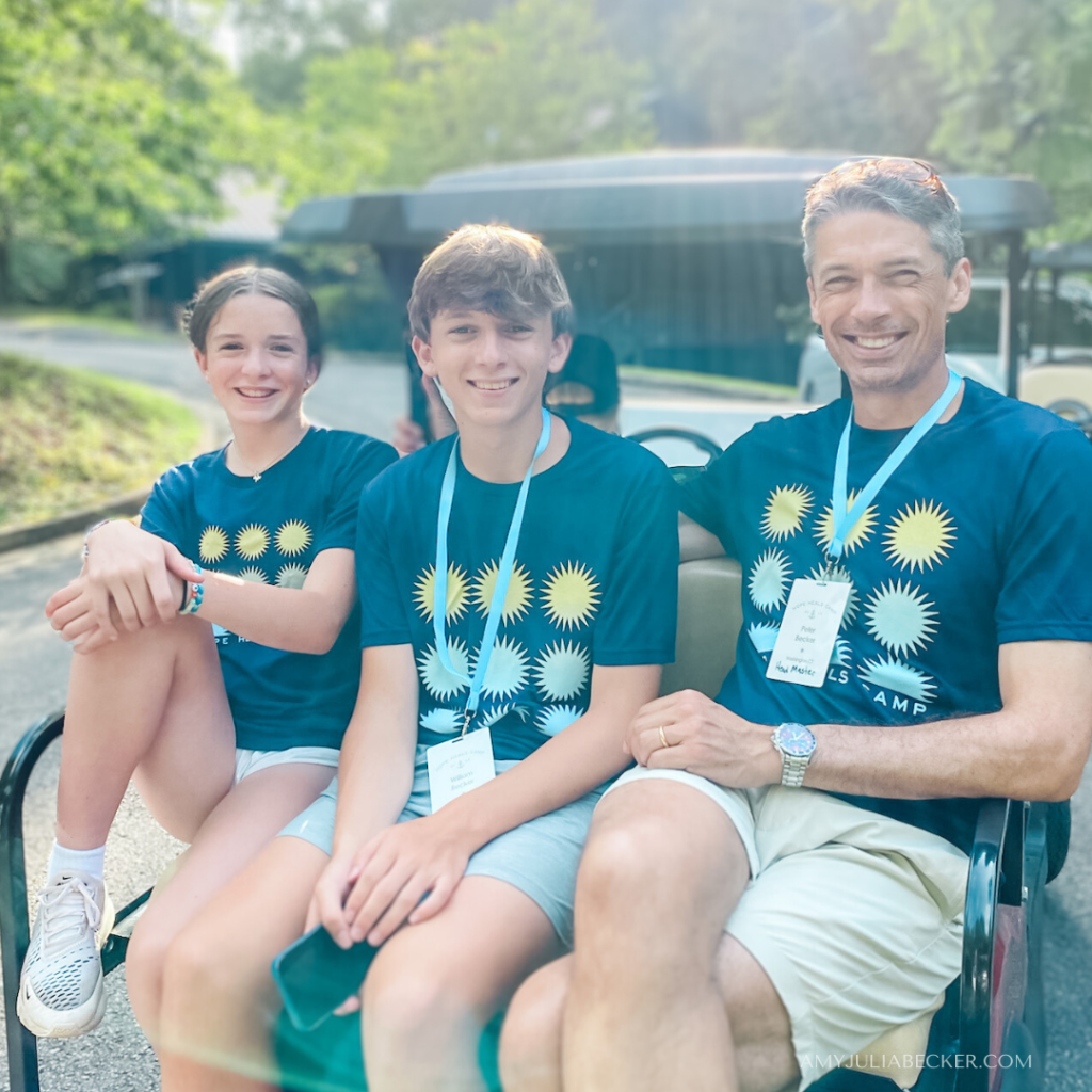 photo of Marilee, William, and Peter all wearing Hope Heals Camp t-shirts and sitting on the back of a golf cart