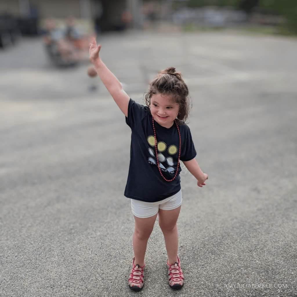 photo of a six-year-old girl standing outside, smiling, and raising her hand