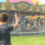 photo of a young teen pointing to a colorful carousel