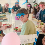 photo of William with family and friends sitting at a large white table for a birthday party