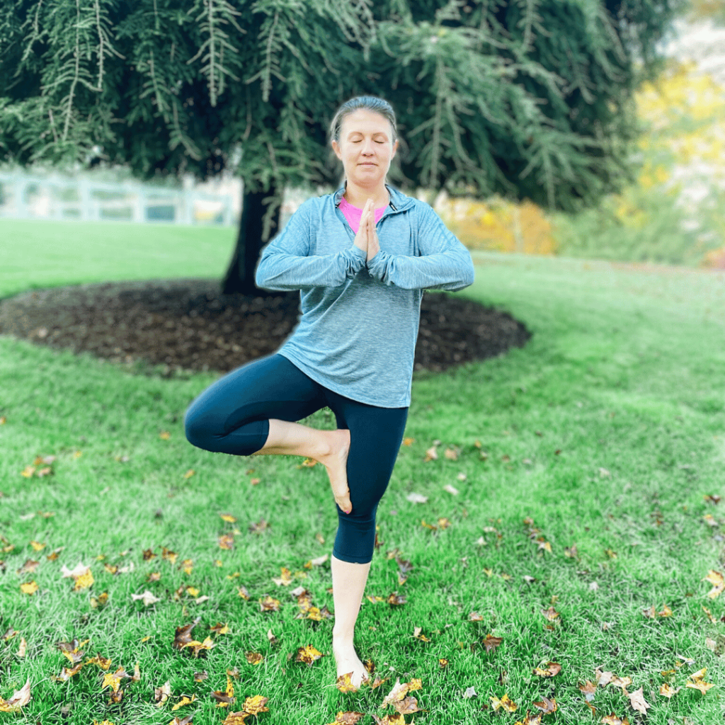 Amy Julia practices the tree pose outside near a tree