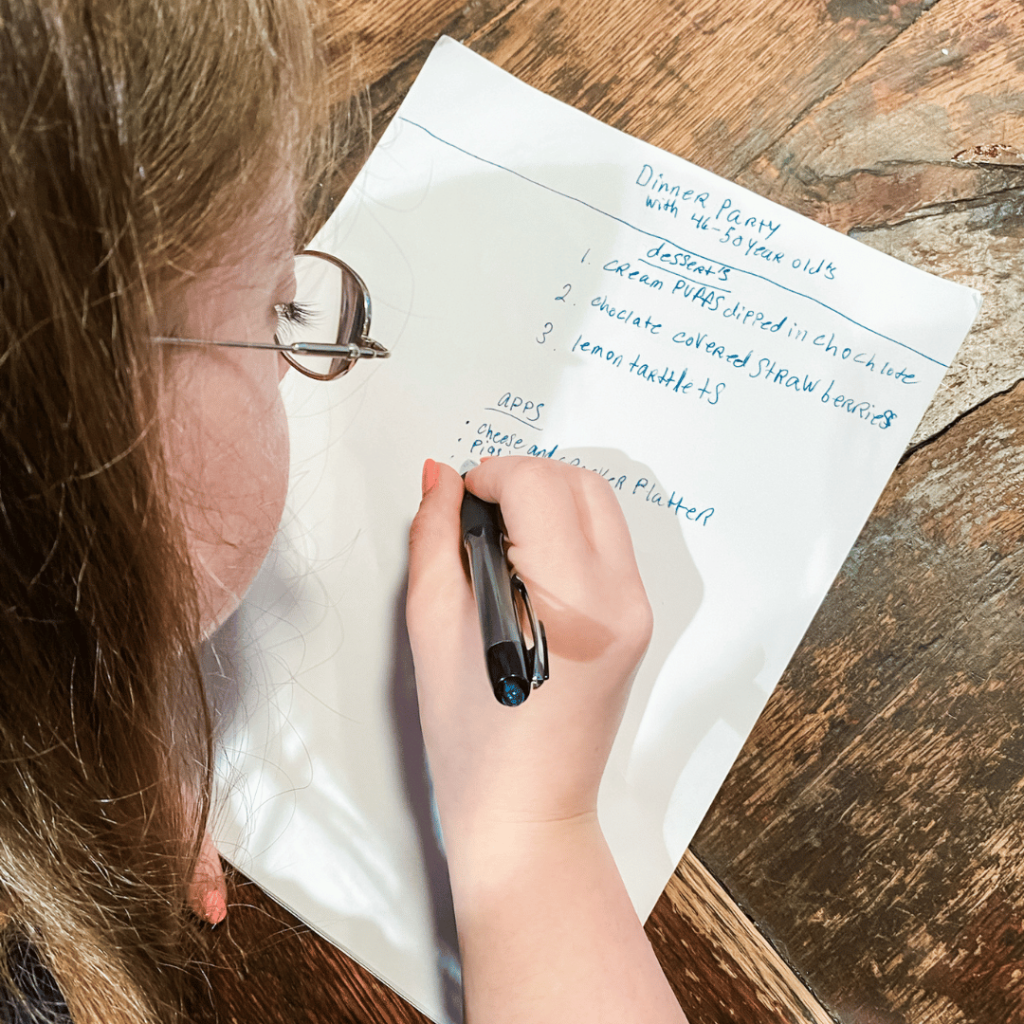 photo of Penny looking down at a wooden table and writing a list on a piece of paper