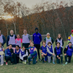 photo of a soccer team posing in front of fall trees with the sun setting behind them