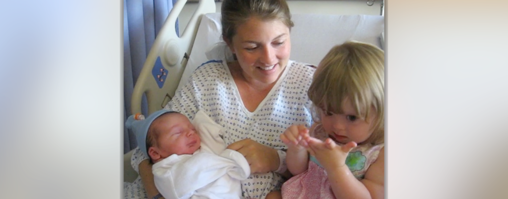 Amy Julia sits in a hospital bed and hold baby William and toddler Penny