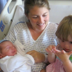 Amy Julia sits in a hospital bed and hold baby William and toddler Penny