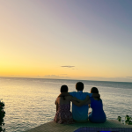 photo of Amy Julia's three teenagers sitting on a stone wall with their arms around each other and looking away from the camera out at the ocean in front of them