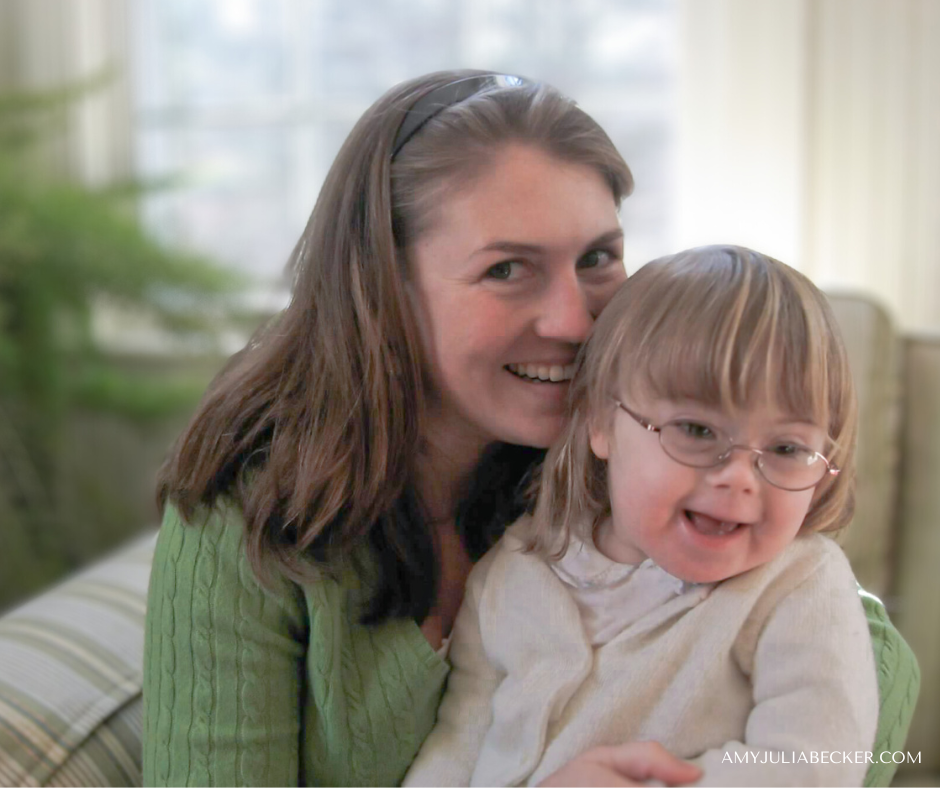 photo of Amy Julia sitting on a couch and smiling at the camera with toddler Penny in her lap, who is also smiling