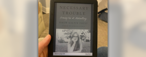photo of Amy Julia's hand holding a kindle with the book Necessary Trouble on the cover