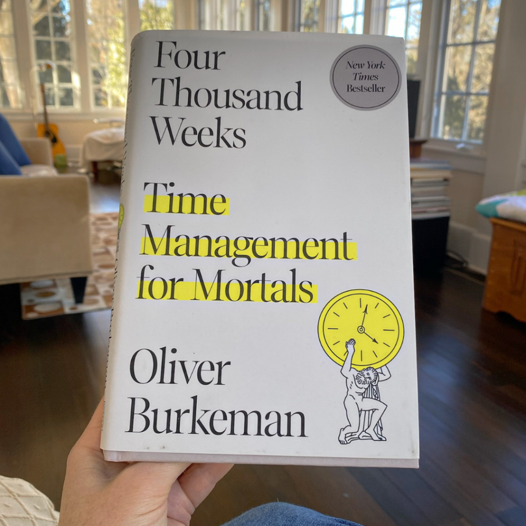 A hand holds up the book Four Thousand Weeks (the book cover is white with the title and author's name, Oliver Burkeman, in black text, with the words "Time Management for Mortals" highlighted in yellow. In the right bottom corner, an ancient man struggles to hold up a yellow-highlighted clock.