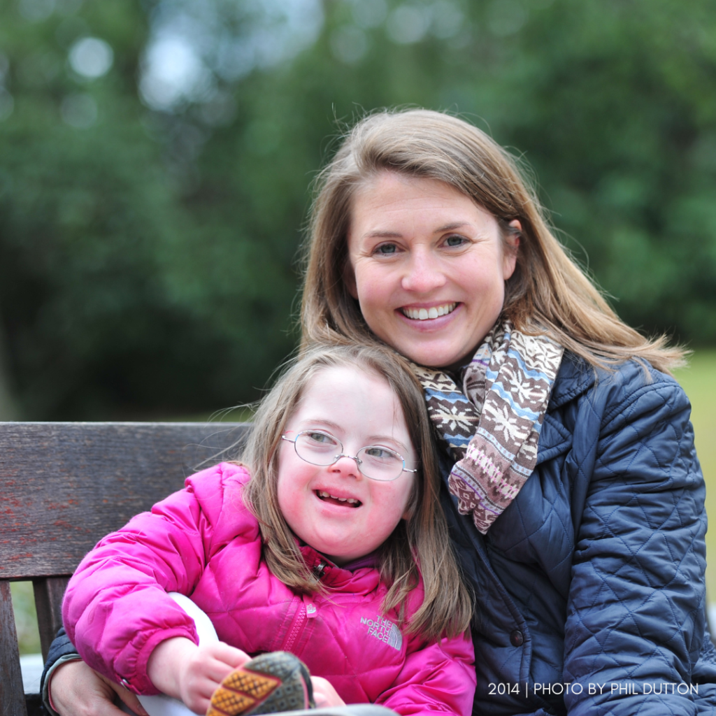 Amy Julia and young Penny from 2014. They are sitting on a wooden bench and are wearing winter coats as they smile at the camera