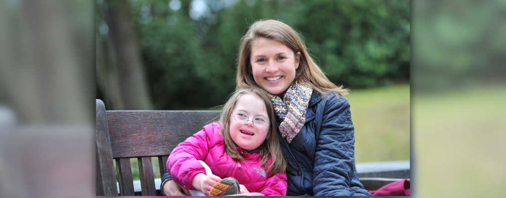 photo of Amy Julia and young Penny from 2014. They are sitting on a wooden bench and are wearing winter coats as they smile at the camera