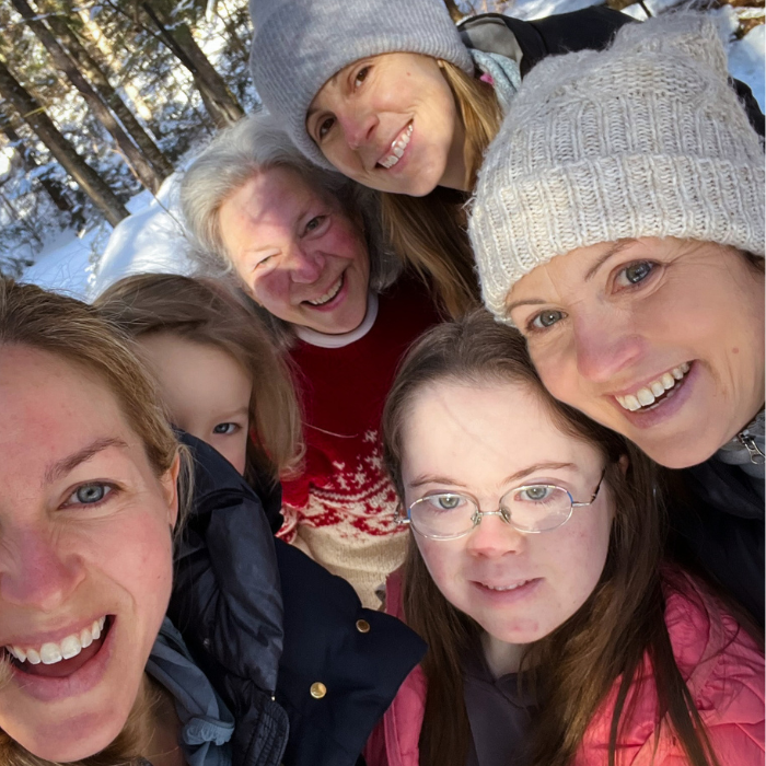 group of women and girls wearing coats and winter hats and smiling for a selfie in the woods