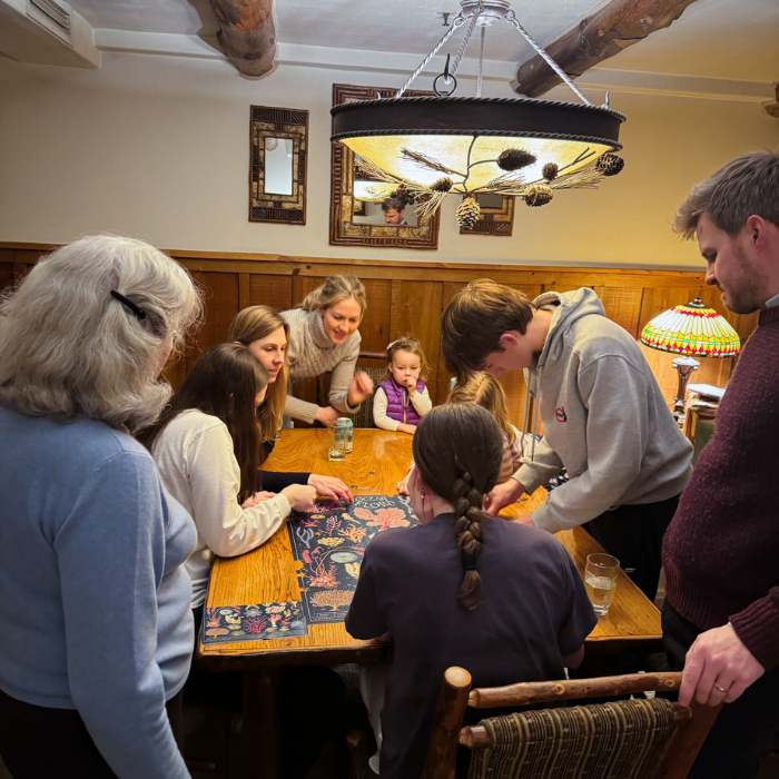 three generations of a family lean over a table putting together a puzzle