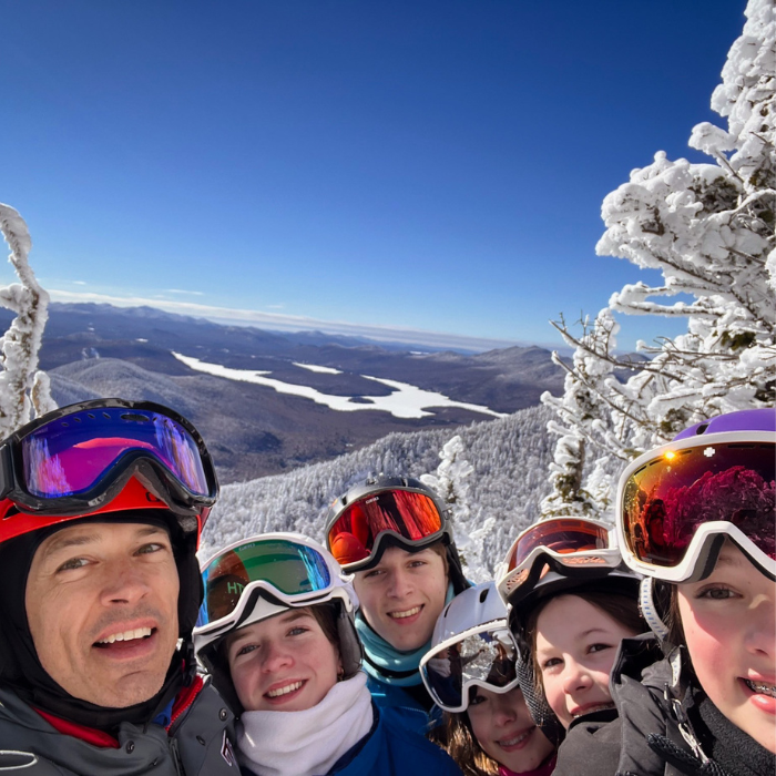 group of snow boarders smiling for a selfie; they are all wearing goggles pushed up on their foreheads