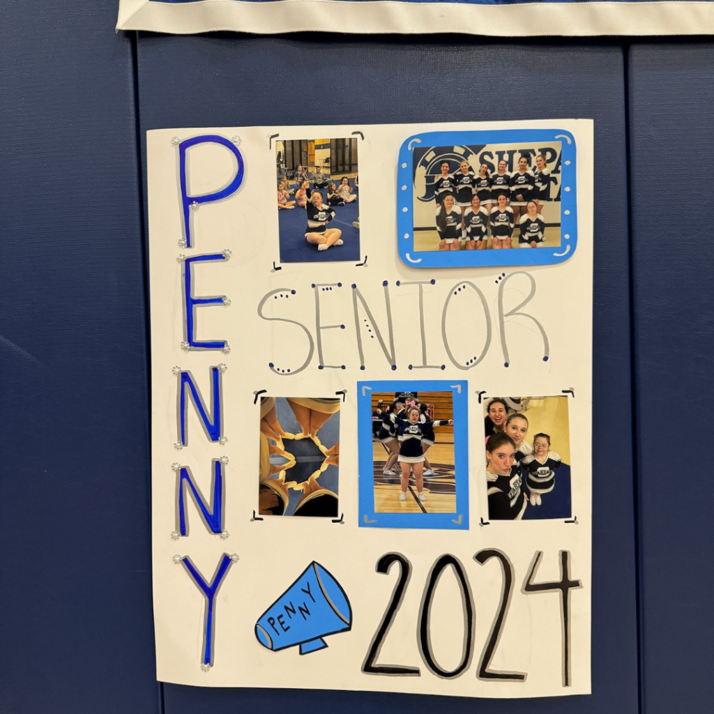 A white sign is on a blue wall and written on the sign is "Penny Senior 2024" Attached to the sign are cheerleading photos.