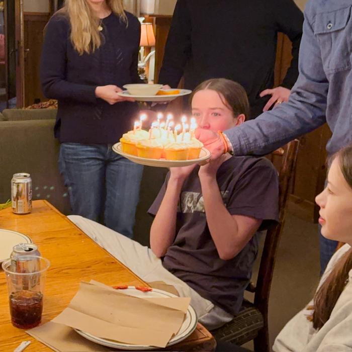 a plate full of lemon cupcakes (each one has a candle) is being lowered to the table in front of the birthday teenager