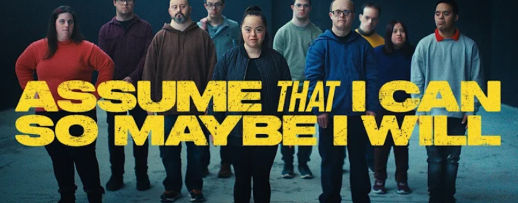 screenshot of "Assume that I can" ad which shows a young woman with Down syndrome surrounded by young men with Down syndrome and yellow text overlay that says, "Assume that I can so maybe I will."