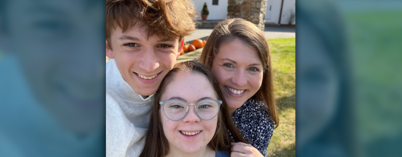 an outdoor photo of William, a teenage boy, Penny, a teenage girl with Down syndrome, and their mom, Amy Julia, leaning in close together and smiling at the camera