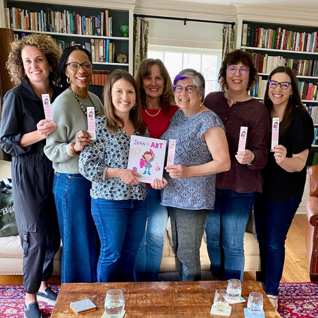 photo of Amy Julia with a group of women; she is holding the children's book Joan of Art