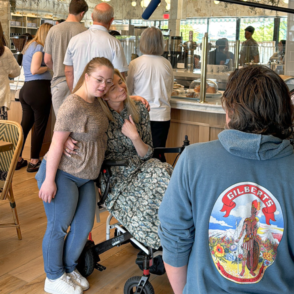 Penny stands next to Katherine Wolf, who is using a wheelchair. They are being interviewed inside Mend Coffee and Goods