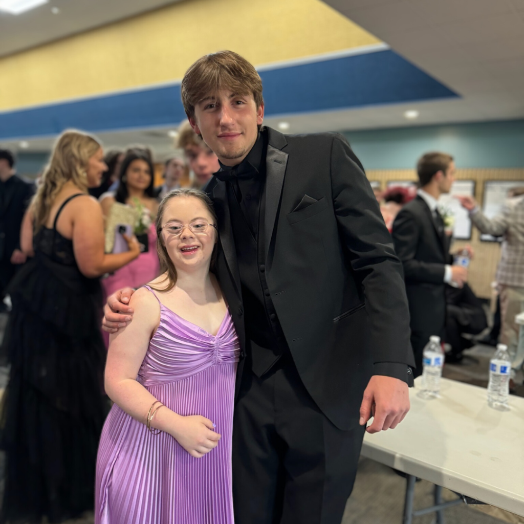an indoor photo of Penny wearing a purple prom dress and posing with a friend