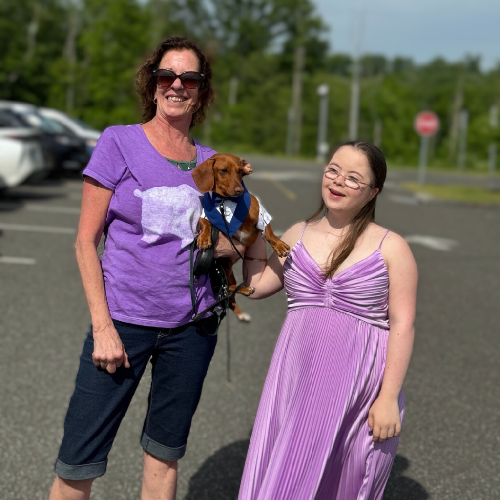 photo in a parking lot of a friend holding a dog and Penny smiling and wearing her prom dress