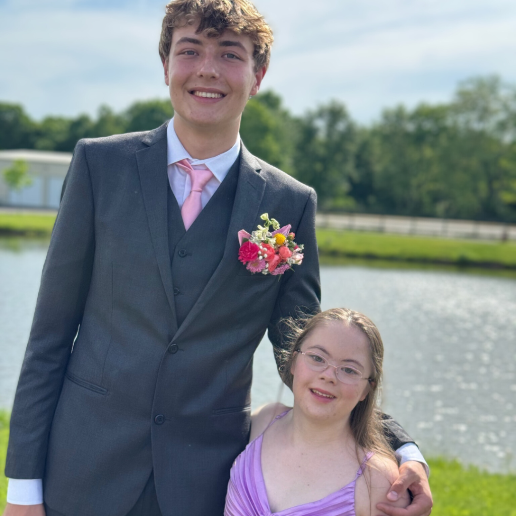 an outdoor photo of Penny wearing a purple prom dress and posing with a friend in front of a pond