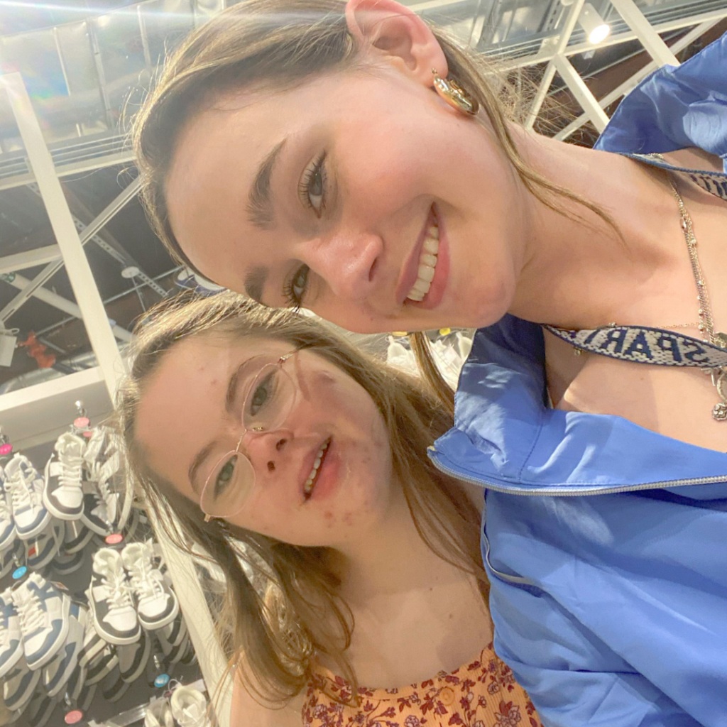 Penny and a friend smiling for a selfie in front of rows of shoes