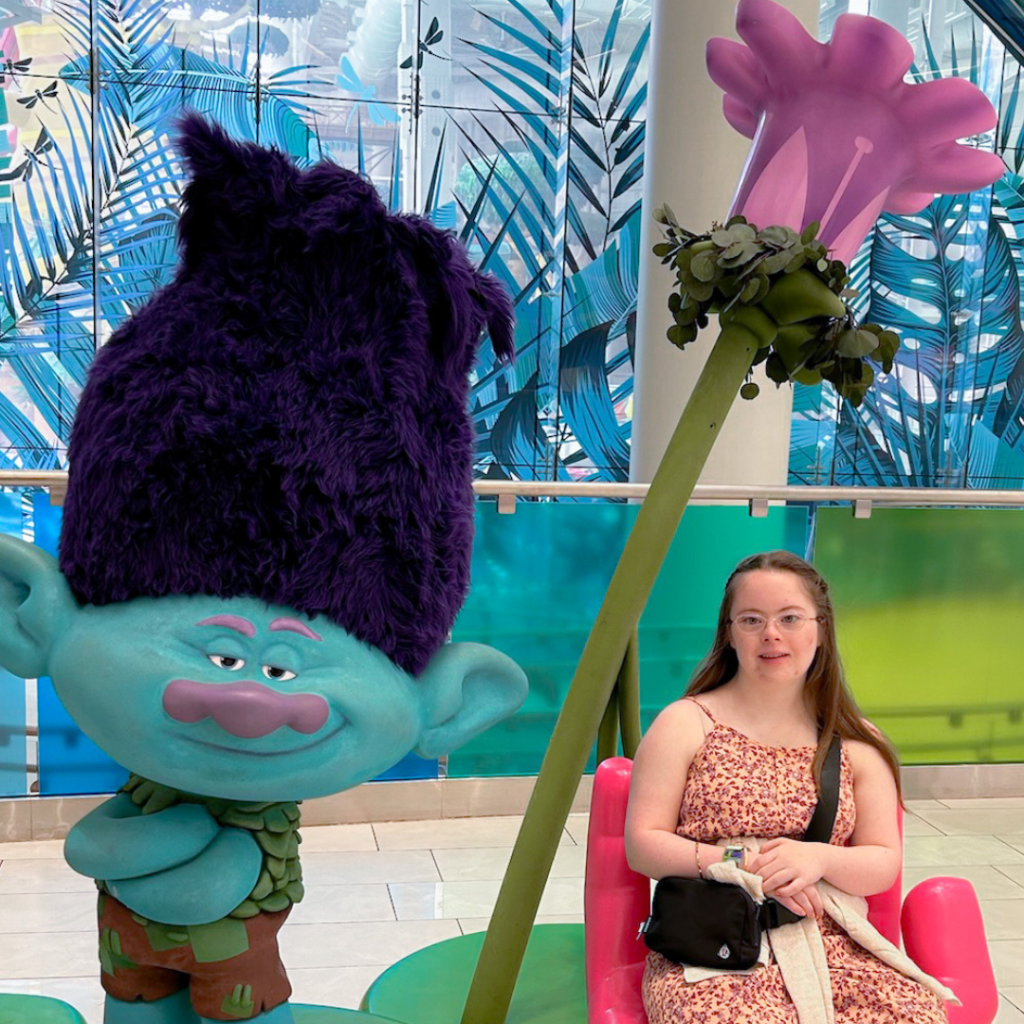 Penny sitting in a chair next to a troll from the movie Trolls