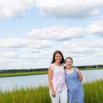 photo of Amy Julia and Penny standing in front of a marsh with water, grass, and blue sky behind them