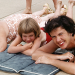 an old photo of two women and a child lying on a beach pad with water behind them
