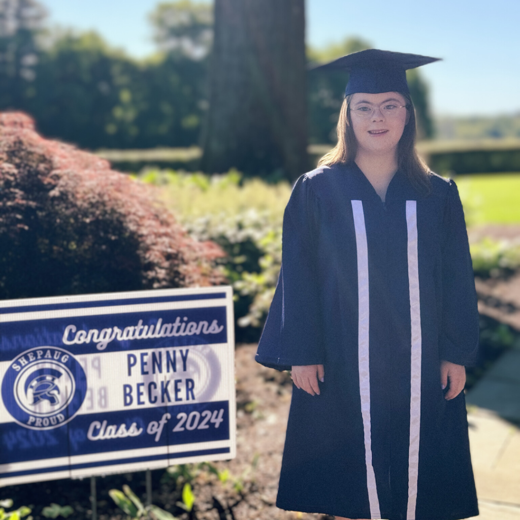 Penny wears her graduation cap and gown and stands next to a sign that says Congratulations Penny Becker Class of 2024