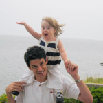 photo from 2008 of Peter holding two-year-old Penny on his shoulders with the ocean in the background]