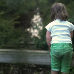 photo of Penny when she was five years old. She is standing on a wooden railing, with her back to the camera, and looking at a blurred creek below