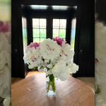 photo of peonies in a vase on a table with a window behind