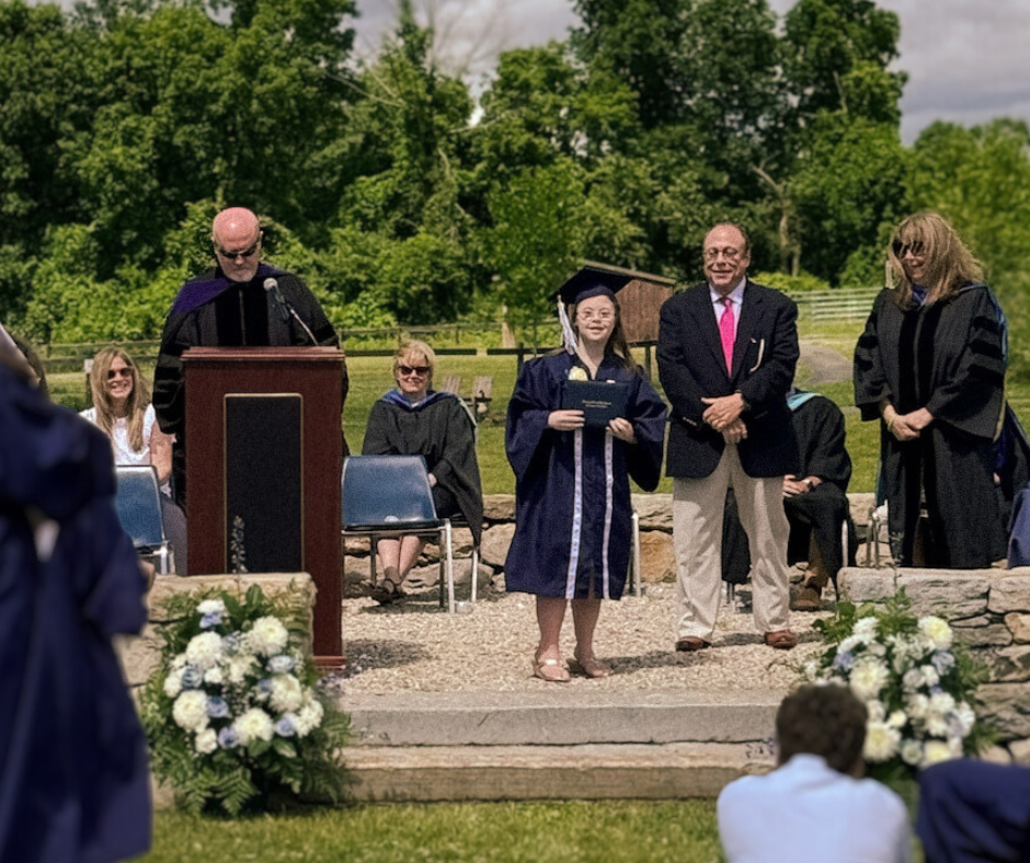 [image description: Penny pauses on stage and looks at the camera after receiving her diploma. She is wearing a graduation cap and gown.]