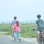 A blurry photo taken from a car of Penny pedaling on a tandem bike behind Peter. William is on another bike behind them.