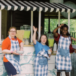 photo of Penny and other teens with disabilities standing in front of a lemonade stand and waving
