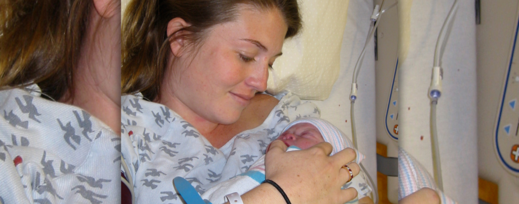 Amy Julia sits in a bed and looks down at baby Penny in her arms