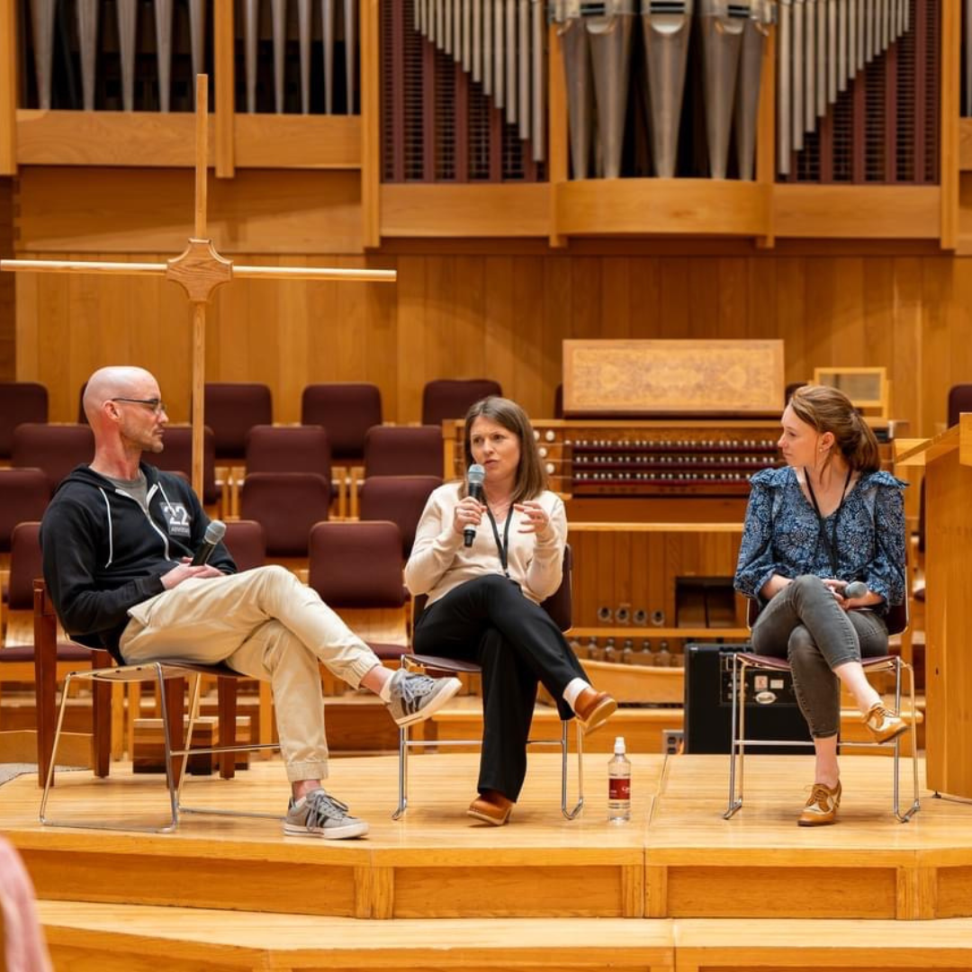 Amy Julia speaks on stage at Calvin University. She is sitting in between a man and a woman.