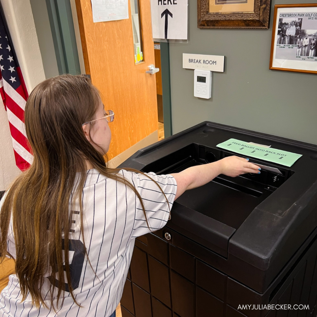 Penny is placing an her ballot into a black ballot drop box.