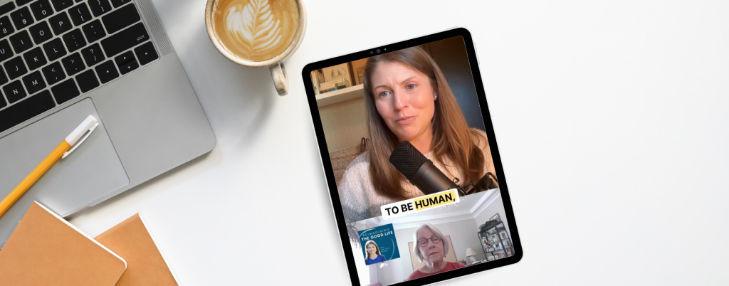 An image featuring a tablet placed on a white desk alongside a laptop, a cup of coffee with latte art, a pencil, and notebooks. The tablet displays a video call, showing two women engaging in a discussion. The top half of the screen shows Amy Julia speaking into a microphone, with the text overlay 'TO BE HUMAN,' while the bottom half features Rosemarie in a smaller window with a background of bookshelves.