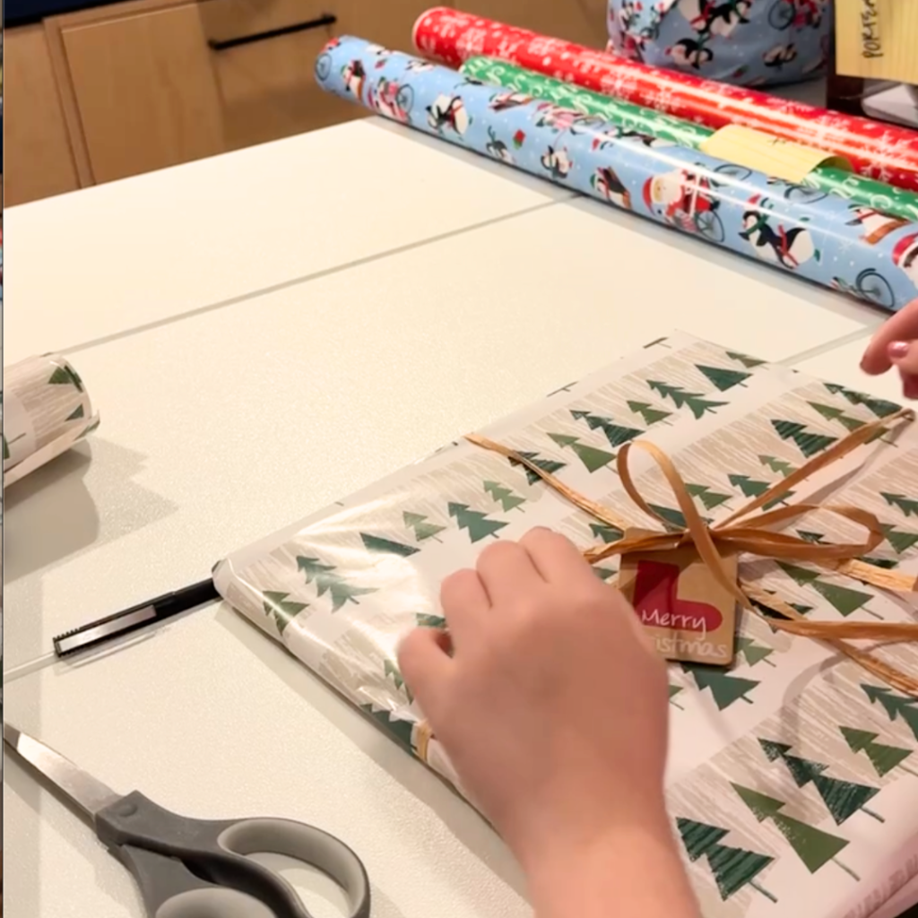 Penny's hands tying a ribbon around a Christmas gift