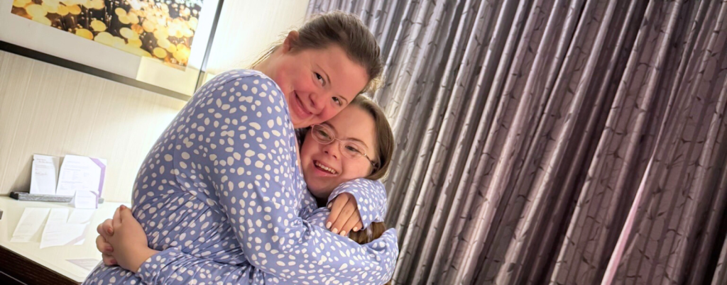 Rachel and Penny are wearing matching blue pajamas with white polka dots are giving each other a hug.