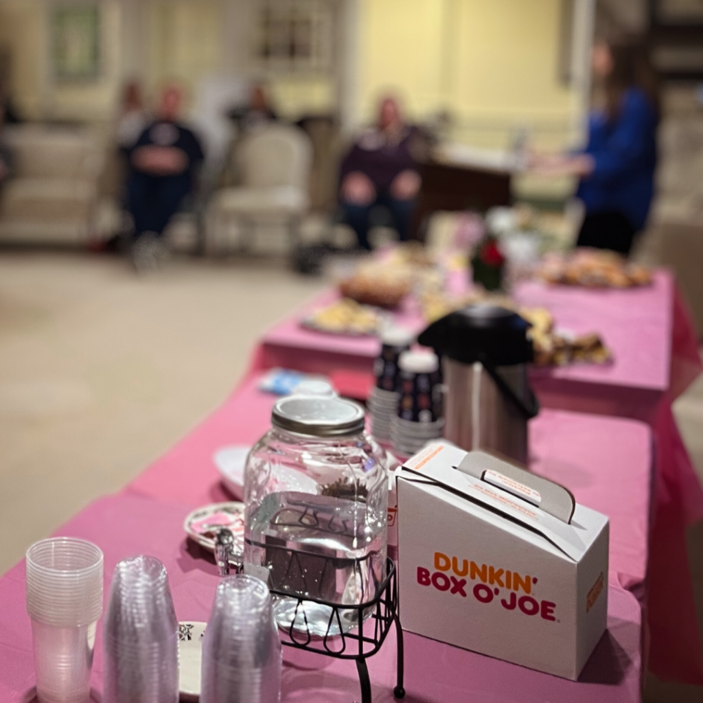 A table covered with a pink tablecloth holds an assortment of refreshments, including pastries and flowers.