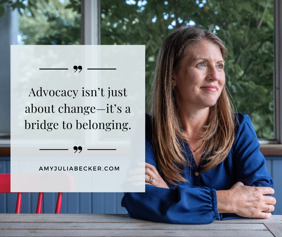 Amy Julia sits at a wooden table and looks off into the distance. Text overlay says: “Advocacy isn’t just about change—it’s a bridge to belonging.”